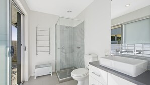 A modern bathroom with a glass shower enclosure, a white toilet, a white sink with a mirror above, and a radiator. - The Lookout 3BR with Ocean views (Apollo Bay)