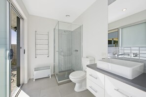 A modern bathroom with a glass shower enclosure, a white toilet, a white sink with a mirror above, and a radiator. - The Lookout 3BR with Ocean views (Apollo Bay)