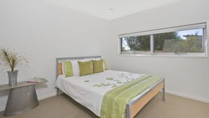 A bedroom with a bed, a window, and a bedside table with a vase.