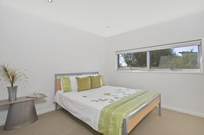 Ein Schlafzimmer mit einem Bett, einem Fenster und einem Nachttisch mit einer Vase.