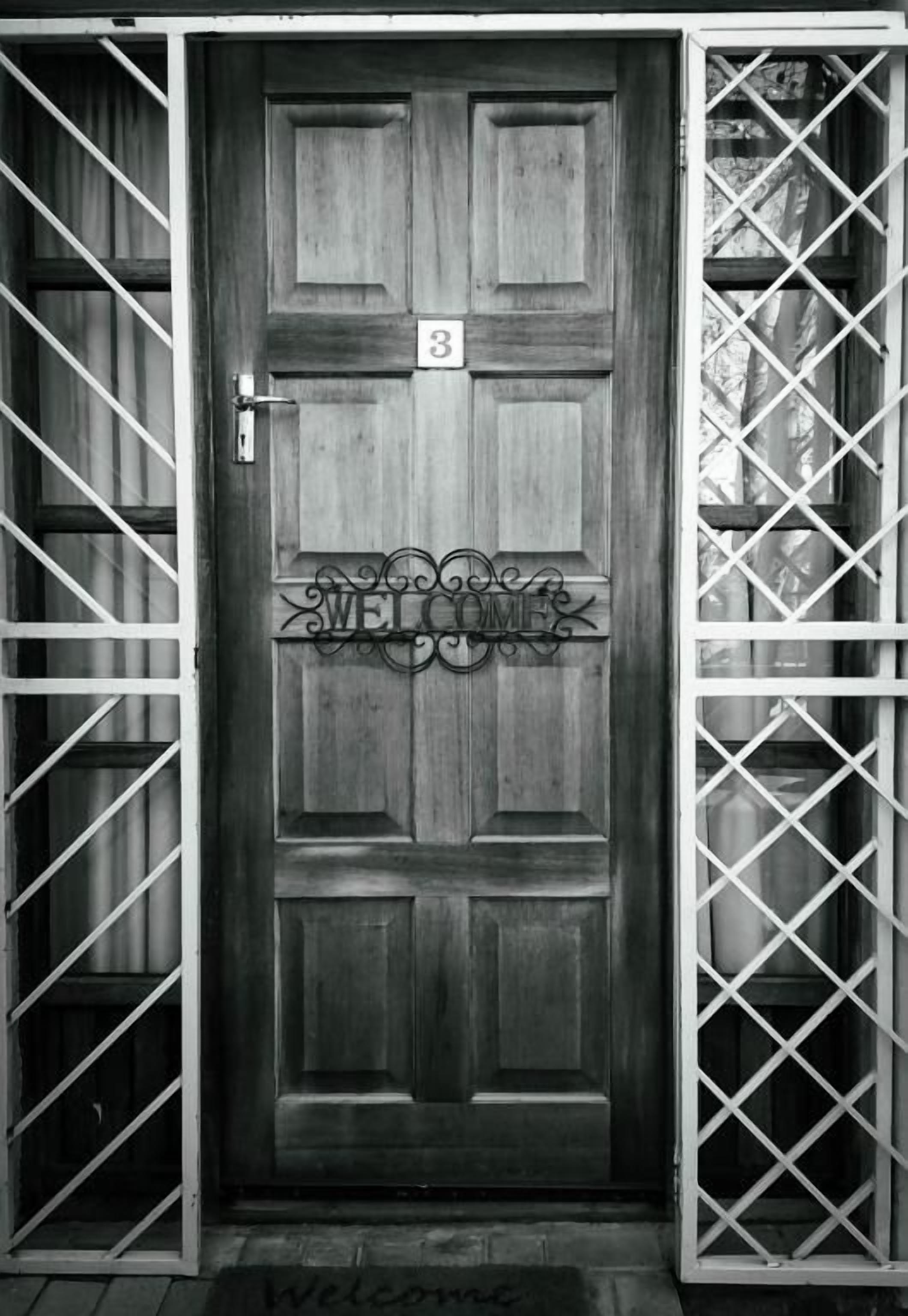 Una puerta de madera con el número '3' y un letrero que dice 'WELCOME', flanqueada por portones metálicos.
