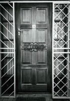 Una puerta de madera con el número '3' y un letrero que dice 'WELCOME', flanqueada por portones metálicos.