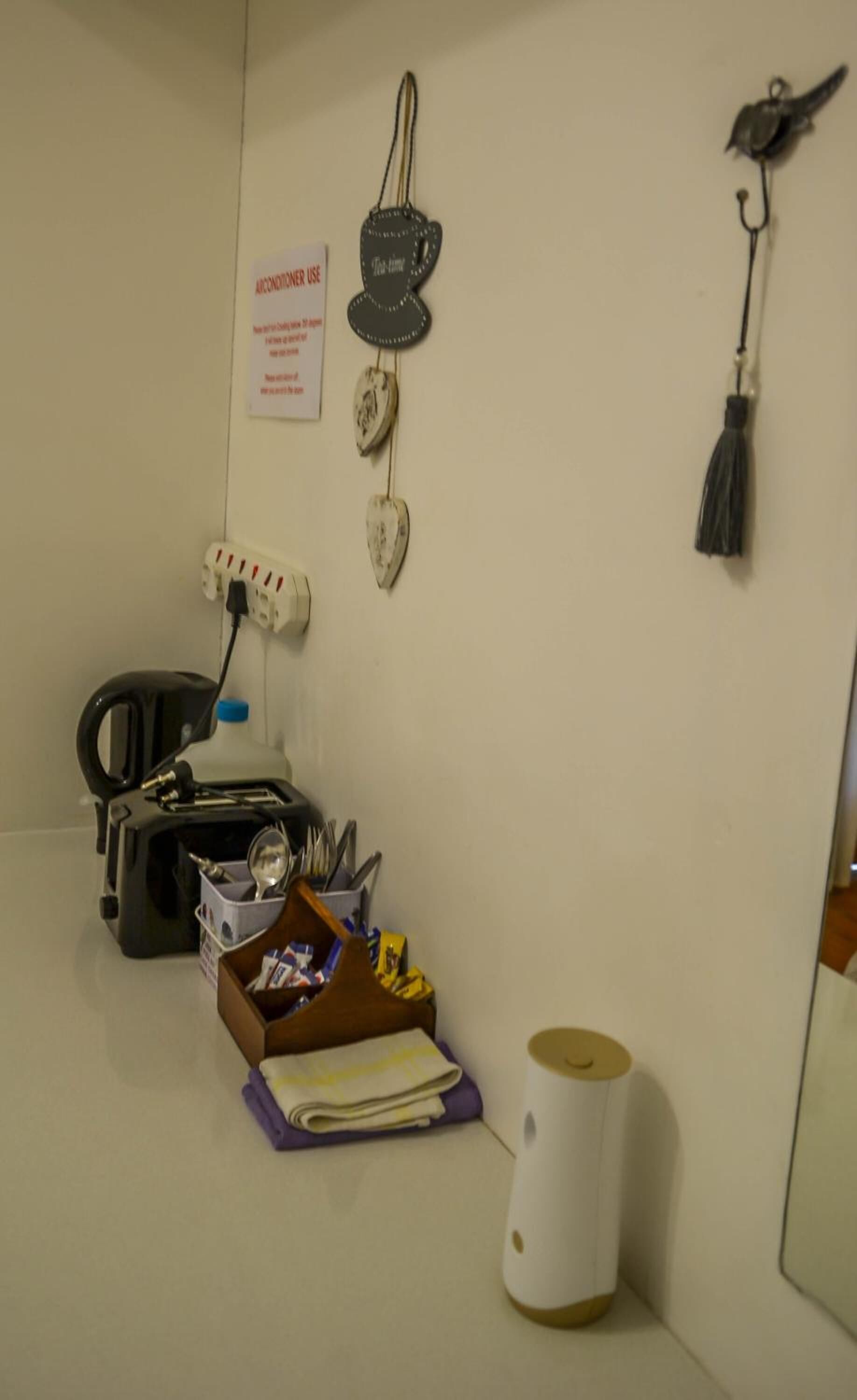 Una habitación pequeña y desordenada con un escritorio, una silla, una tetera, una taza y un cartel en la pared.