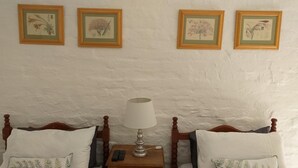 A bedroom with two wooden beds, a bedside table with a lamp, and three framed botanical prints on the wall.