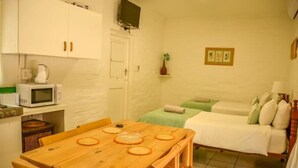 A compact room with a wooden dining table, two single beds, a microwave, and a small kitchen area with a kettle.