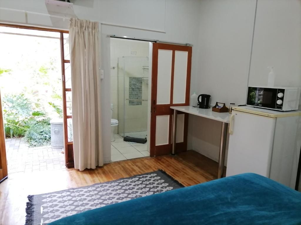 A room with a bed, a small table with a microwave, a shower area, and a view of greenery outside.