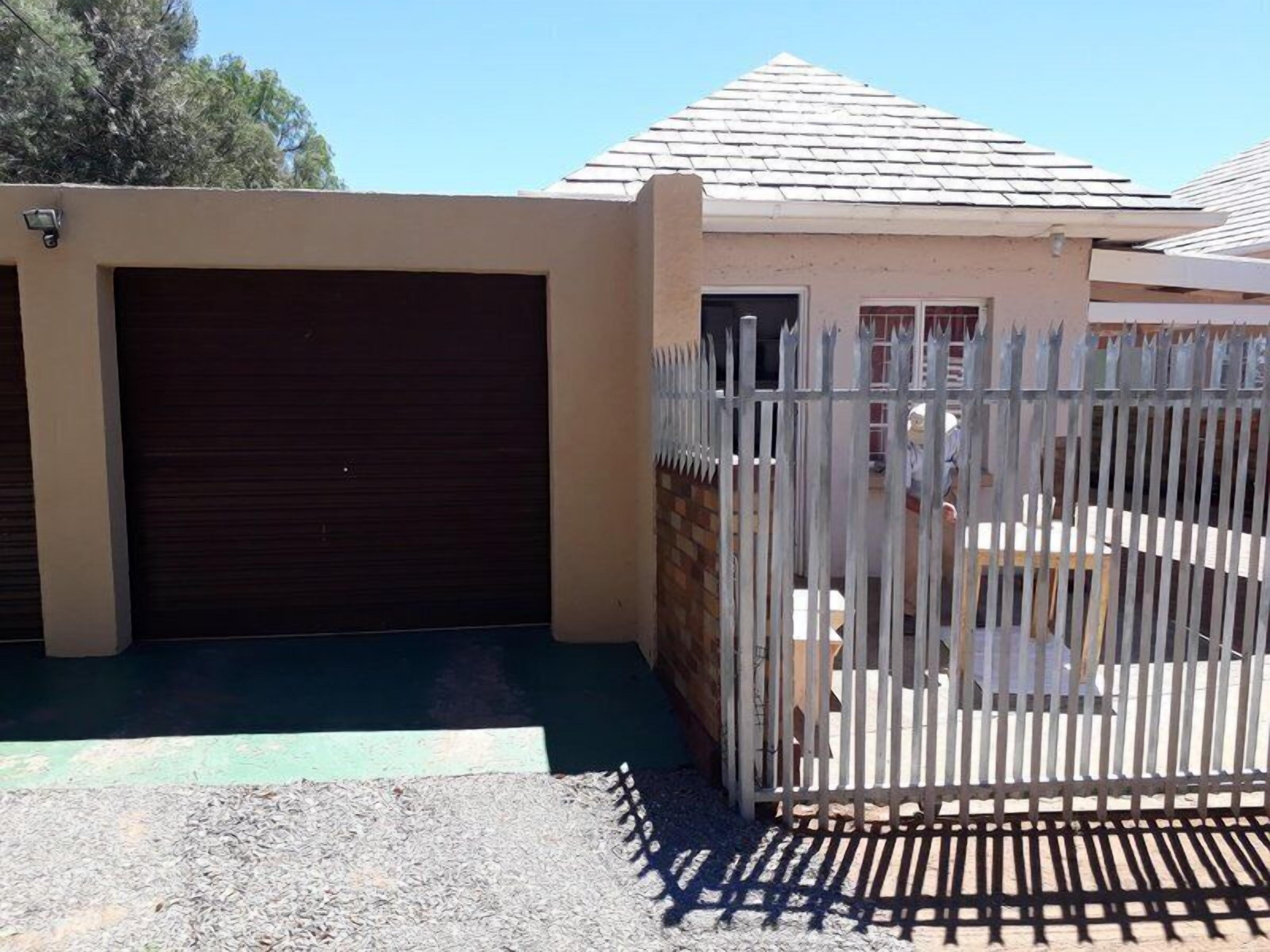 A house with a closed garage door, a fenced yard, and a small building with a sloped roof.