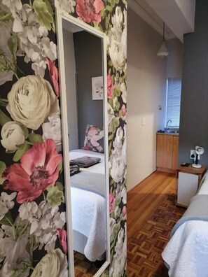 A bedroom with a large mirror, a bed with a white duvet, a wooden floor, and a small bedside table with a lamp. - Padlangs (Kimberley)