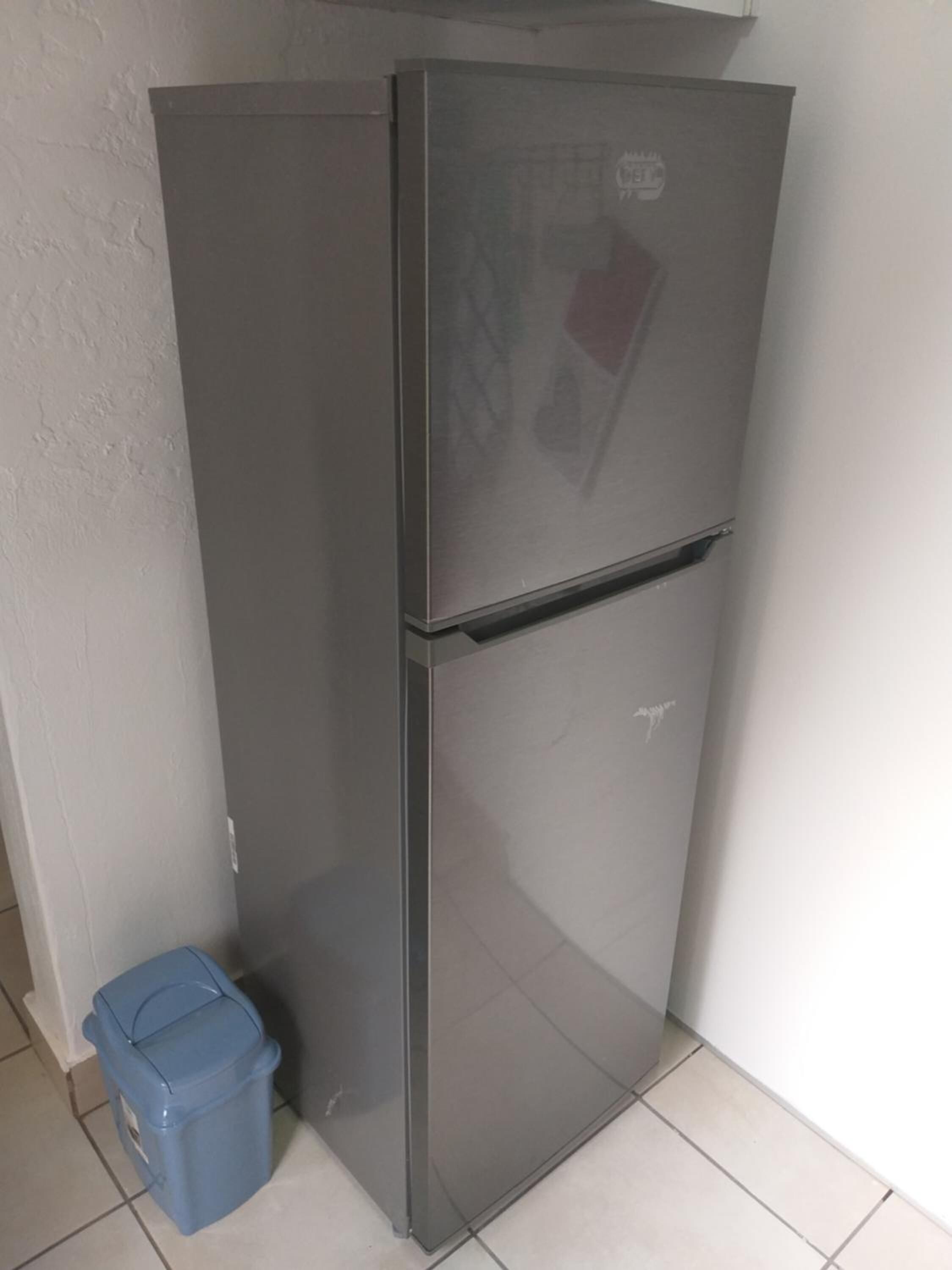 A grey refrigerator with a freezer compartment, located in a corner with a white wall and tiled floor.