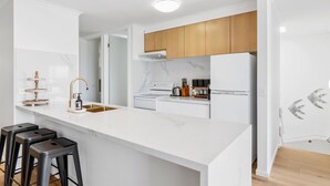 Cozinha moderna com armários brancos, bancada de mármore e uma ilha central com banquetas.