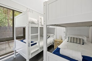 Ein Schlafraum mit Etagenbett, Fenster, Nachttisch und Beistelltisch.