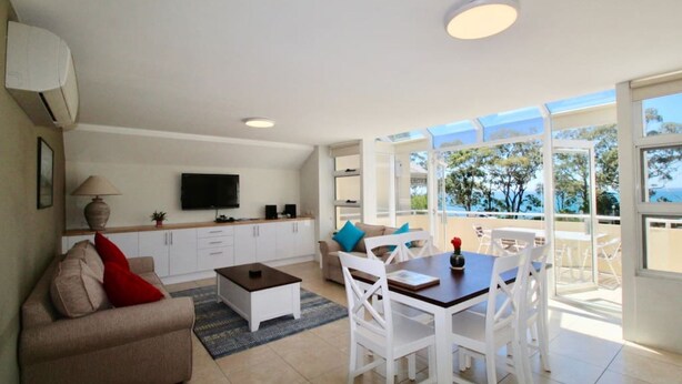 A modern living room with a sofa, coffee table, TV, and a dining area with chairs and a table.