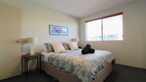 A bedroom with a bed, two bedside lamps, a framed picture on the wall, and a window with blinds.