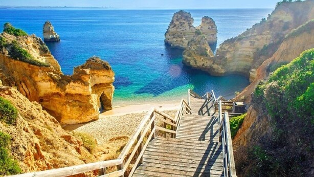 A coastal view with a wooden staircase leading to a beach, surrounded by rocky cliffs and clear blue waters. - Harris Apartment, Pool, Wifi (Lagos)