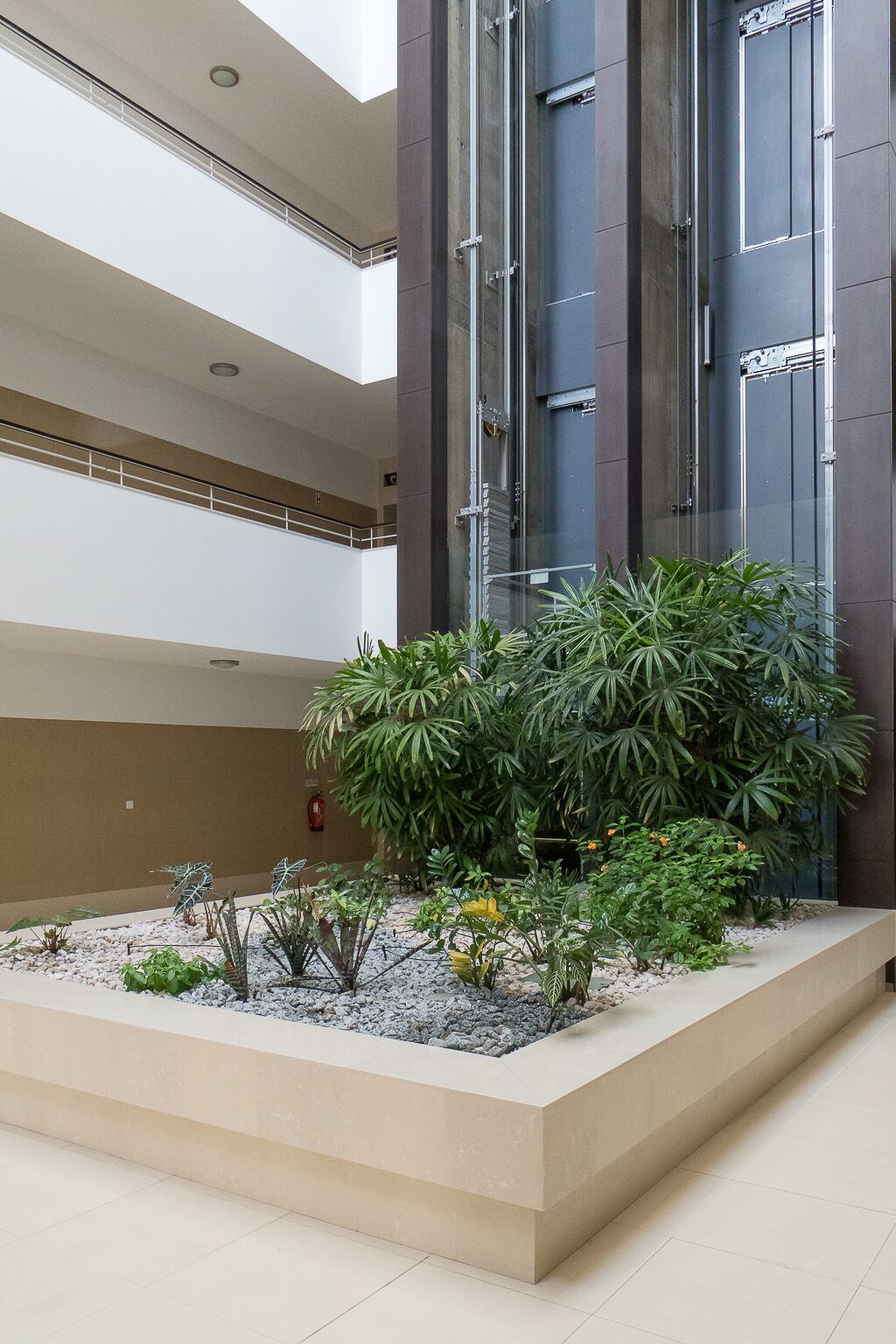 A multi-level building with a central atrium featuring a landscaped garden with various plants and a fire extinguisher on the wall.