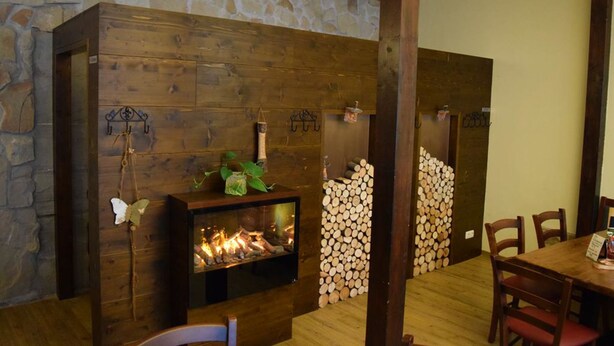 A cozy room with a stone wall, wooden paneling, a fireplace, and a dining area with chairs and a table. - Friedrichshof Restaurant & Pension (Bad Klosterlausnitz)