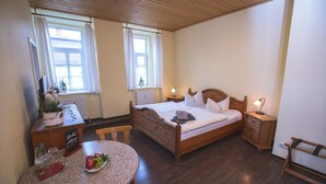 A bedroom with a wooden bed, bedside tables, a desk, and a round table with fruits. - Friedrichshof Restaurant & Pension (Bad Klosterlausnitz)
