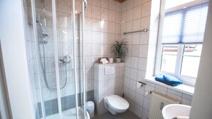 A bathroom with a glass shower enclosure, a toilet, a sink, and a window with blinds. - Friedrichshof Restaurant & Pension (Bad Klosterlausnitz)