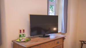 A television on a wooden cabinet with two bottles of wine and a plate of food. - Friedrichshof Restaurant & Pension (Bad Klosterlausnitz)