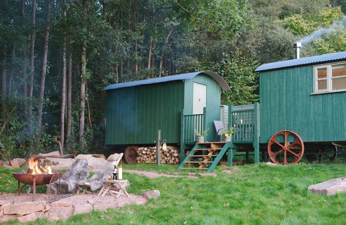 A rustic cabin with a green exterior, a fire pit, and a wooden wheel.