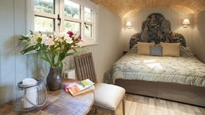 A bedroom with a bed, a bedside table with a vase of flowers, a chair, and a lamp.