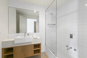 A modern bathroom with a white sink, mirror, and glass shower enclosure. - Sandy Beach Apt 6 (Lorne)