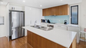A modern kitchen with white cabinetry, a stainless steel refrigerator, a double sink, and a microwave.