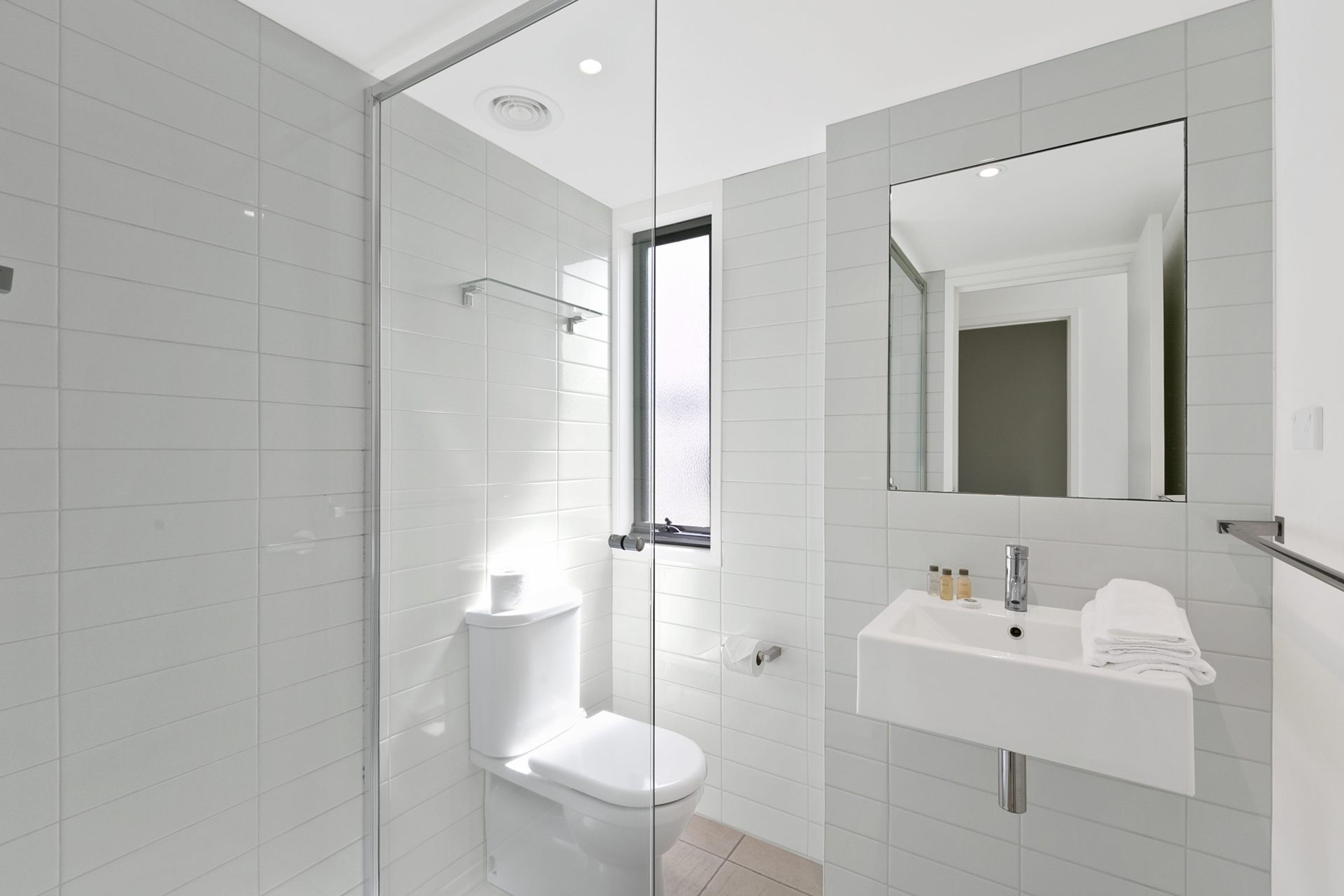 A modern bathroom with a glass shower enclosure, a toilet, a sink with a mirror, and a towel rack.