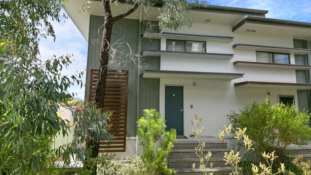 A modern two-story building with a flat roof, a front door, and a staircase leading to the entrance.