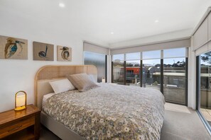 A bedroom with a large bed, a nightstand, and wall art. - Sandy Beach Apt 6 (Lorne)