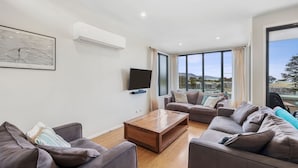 A modern living room with a flat-screen TV, two sofas, a coffee table, and a large window offering a view of the city.