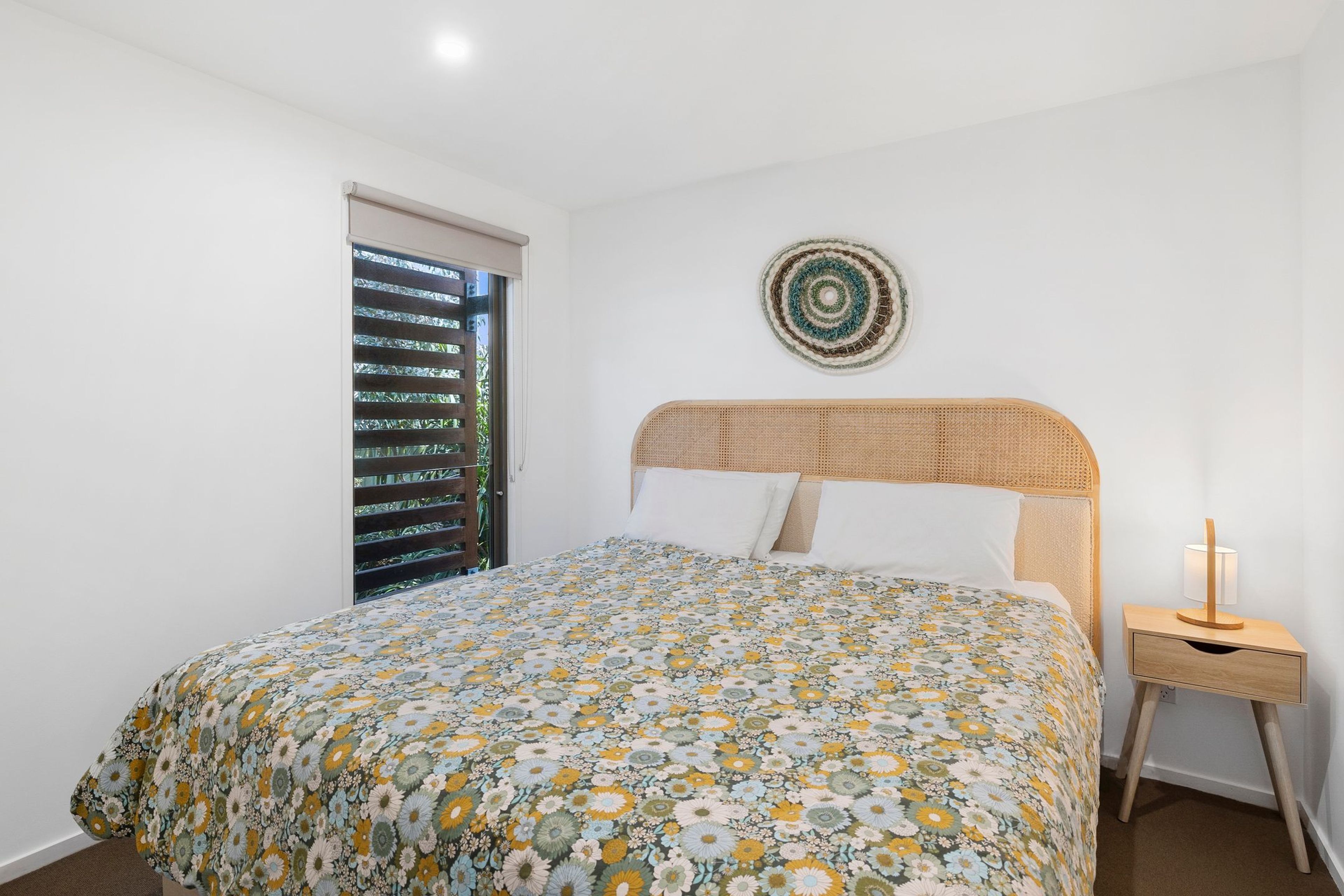 Une chambre à coucher avec un lit, une table de chevet, une décoration murale et une fenêtre avec des stores.