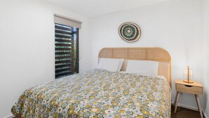 A bedroom with a bed, a bedside table, a wall hanging, and a window with blinds.