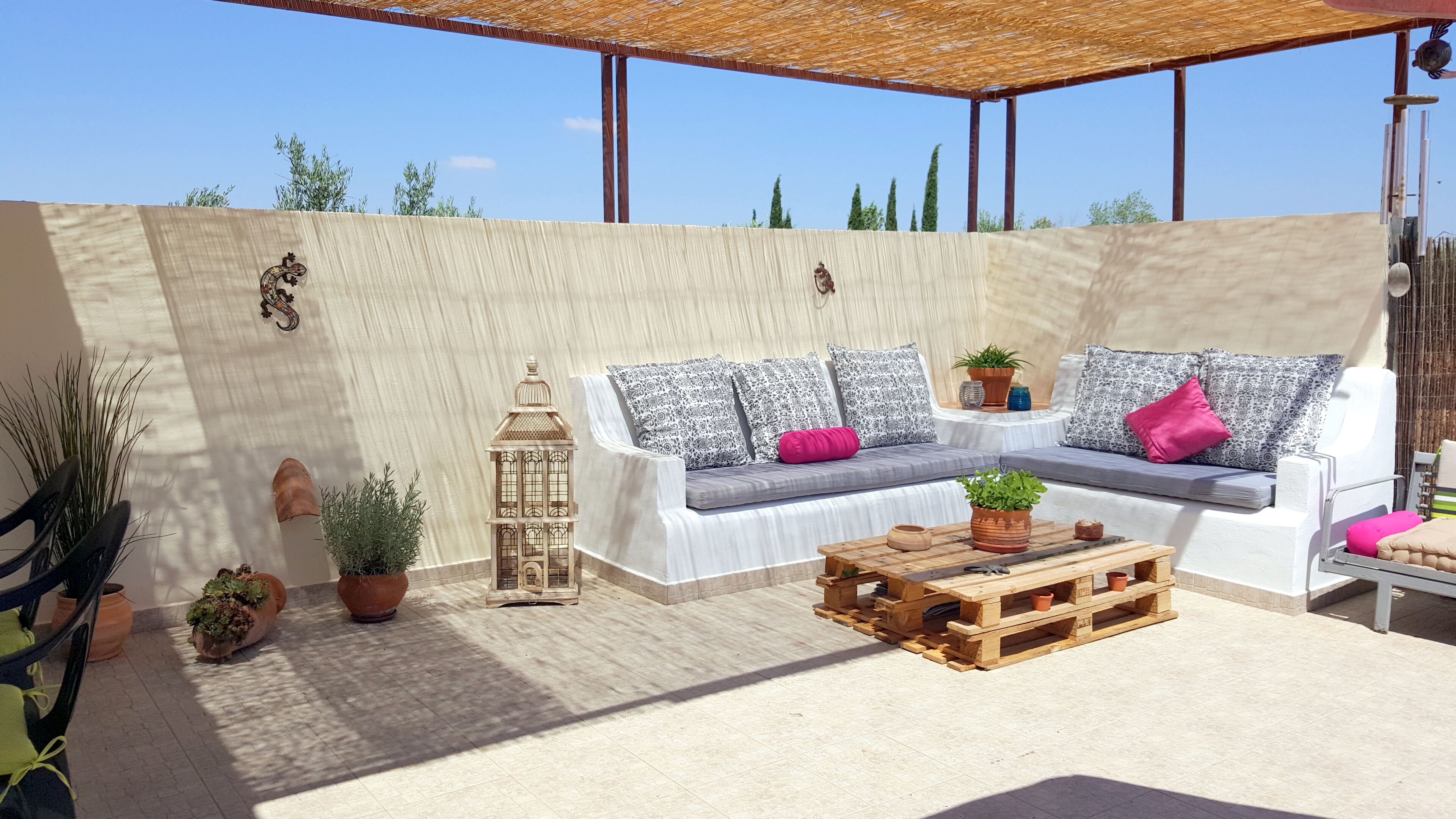 Un espace extérieur aménagé avec un salon de jardin, comprenant un canapé blanc, une table basse en bois et des plantes en pot.