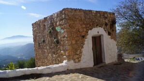 Un bâtiment en pierre, à l’extérieur blanc et doté d’une porte en bois, situé sur une colline et offrant une vue sur des montagnes lointaines.