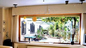 Un salon avec une grande fenêtre donnant sur un jardin. On y trouve un canapé, une table et un radiateur.