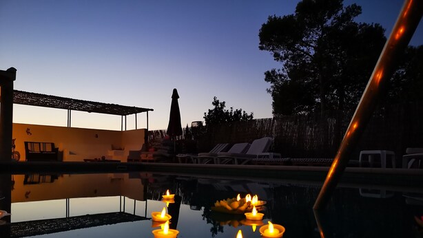 Un espace aménagé au bord de la piscine, avec des chaises longues et une piscine illuminée par des bougies.