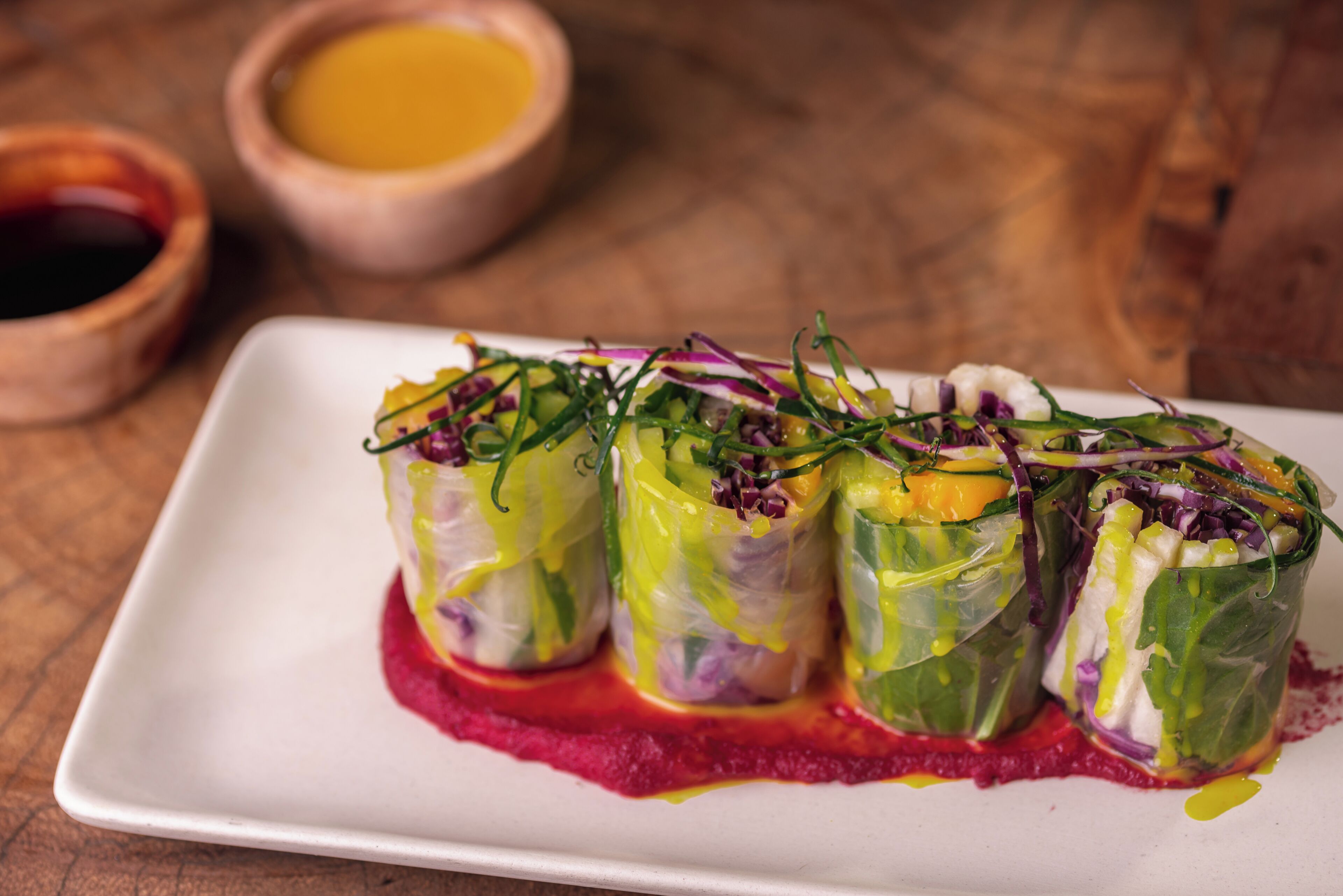 A plate of spring rolls with a red sauce, accompanied by small bowls of sauces.