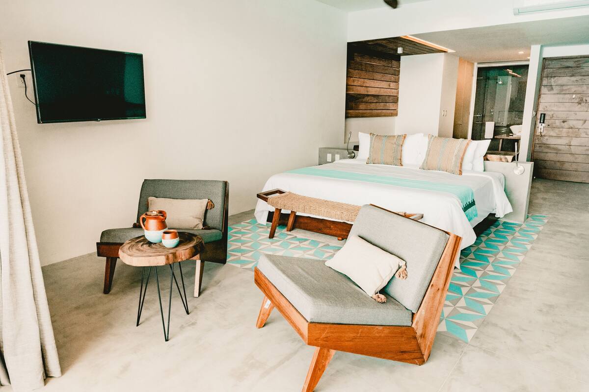 A modern hotel room with a large bed, a seating area with a small table, and a television mounted on the wall.