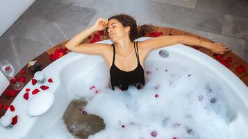 Una persona relajándose en una bañera llena de burbujas y pétalos de rosa.