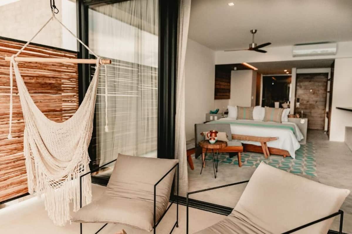 A modern hotel room with a hammock, a bed, a desk, and a chair.