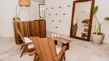 A wooden reception desk with a mirror, a bench, and chairs in a modern room with a tiled floor and potted plants.