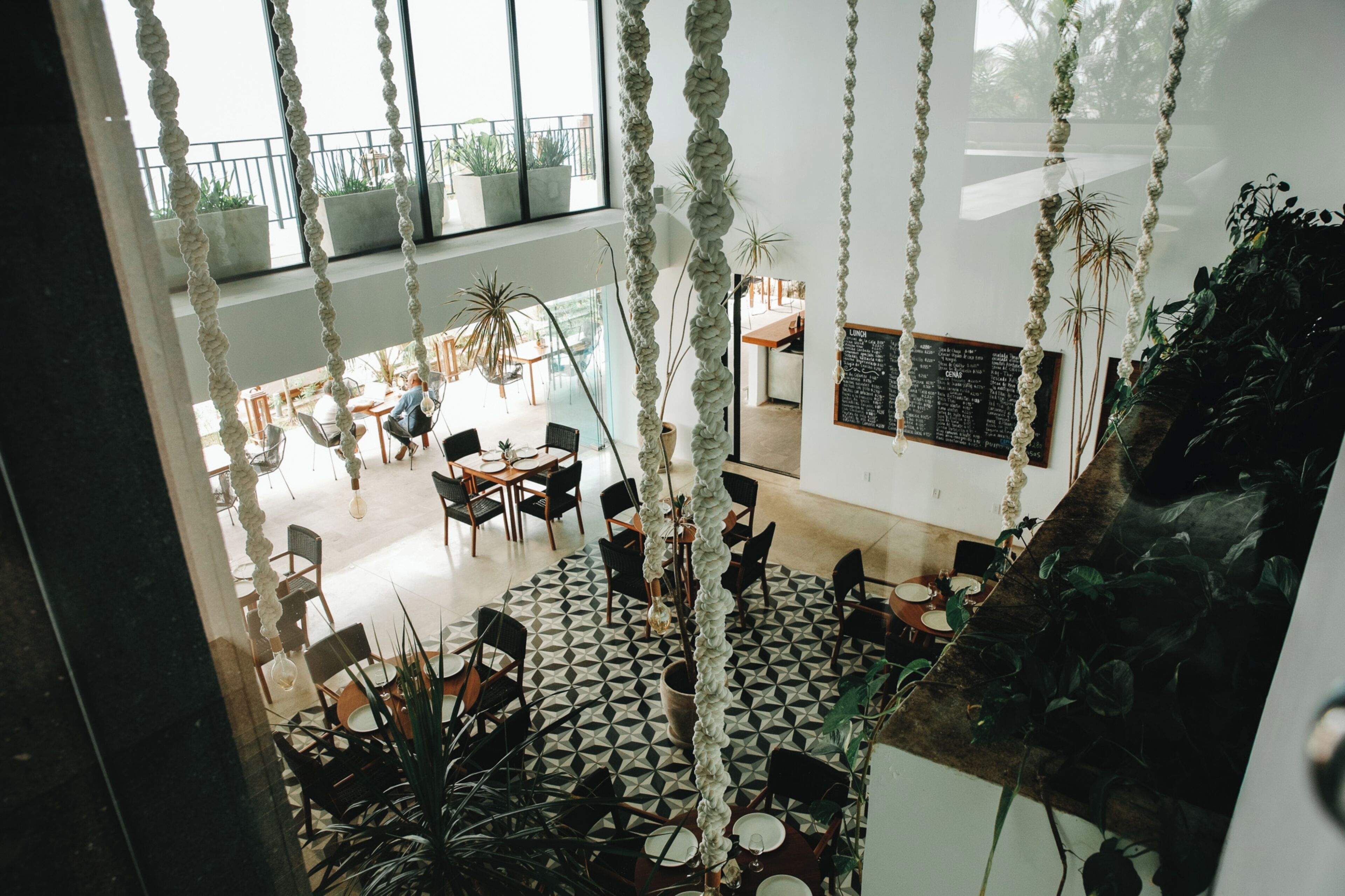 A spacious indoor area with high ceilings, geometric patterned flooring, and hanging rope decorations.