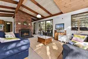 A cozy living room with a fireplace, comfortable seating, and a large window offering a view of the outdoors. - Aireys 15 (Aireys Inlet)