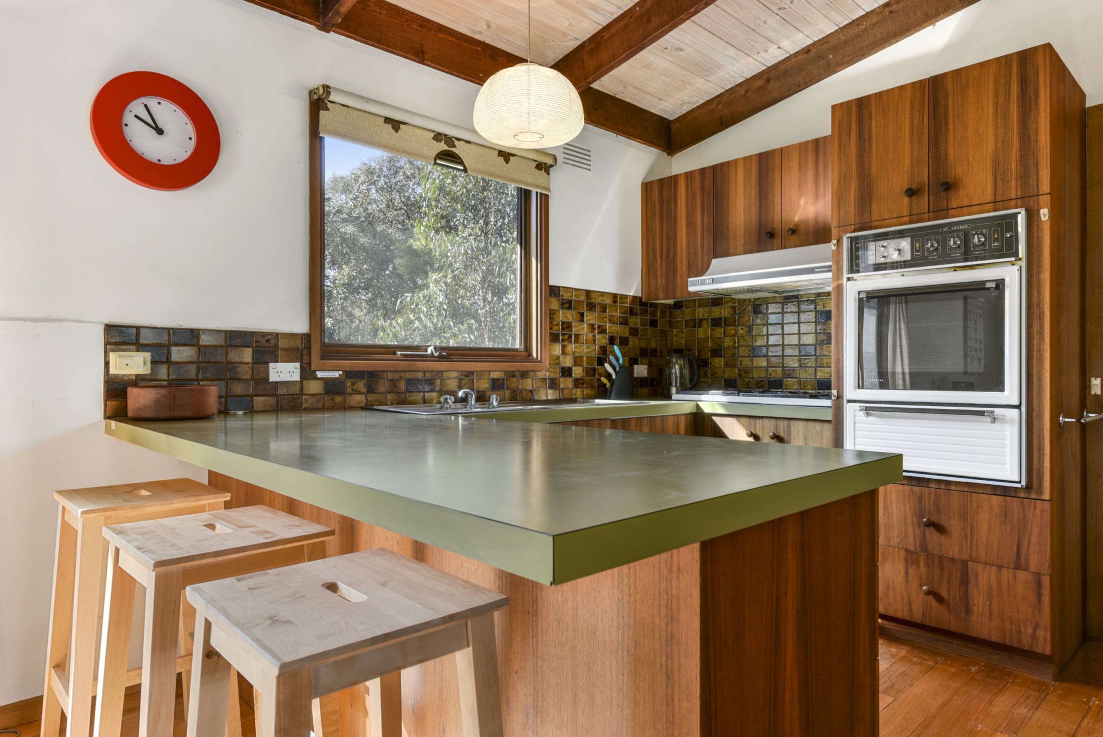 A kitchen with a large island, wooden cabinets, a built-in oven, and a window with a view of trees.