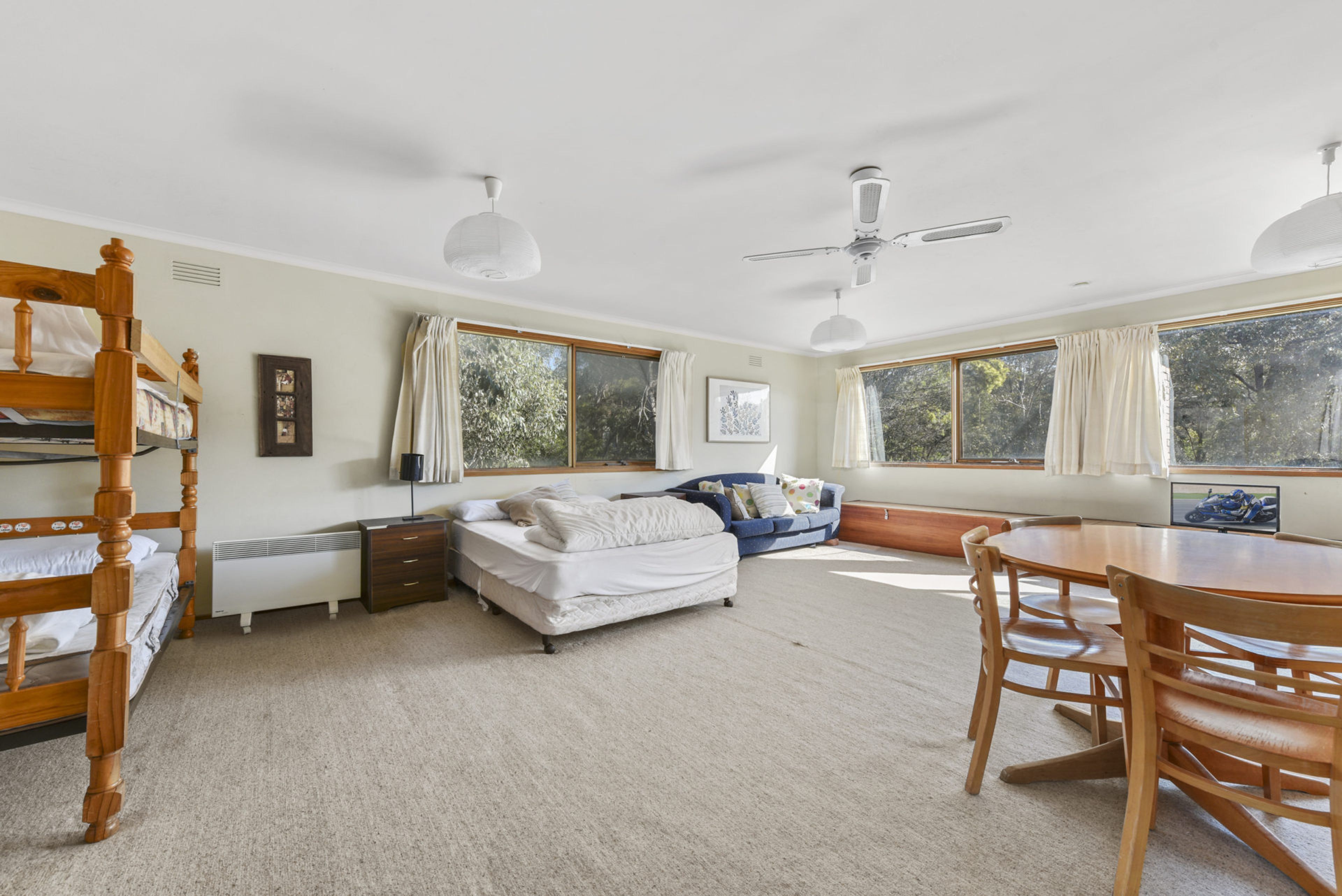 A bedroom with a bunk bed, a single bed, a sofa, a dining table, and a ceiling fan.