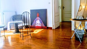 A room with a wooden floor, a black metal chair, a patterned sofa, a painting on the wall, and a small table with glasses. - L'Atelier | Vedi Napoli ai tuoi piedi  (Napoli)