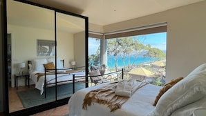 Una camera da letto con un letto grande, vista sul mare e una porta a vetri scorrevoli che dà su un balcone.