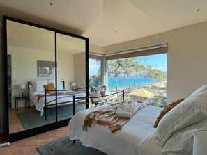 Een slaapkamer met een groot bed, uitzicht op zee en een schuifdeur naar een balkon.