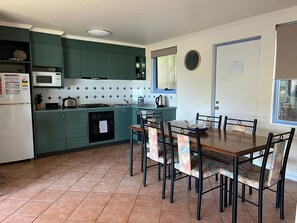 A kitchen with green cabinets, a white refrigerator, a microwave, a stove, and a dining table with chairs. - Vista Di Mare (Lorne)